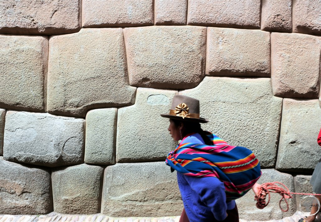A Quechua woman passes in front of a wall of multi-angled stones, a prime example of Inca masonry, in the Hatun Rumiyoc street of Cusco, the former capital of the Inca empire.