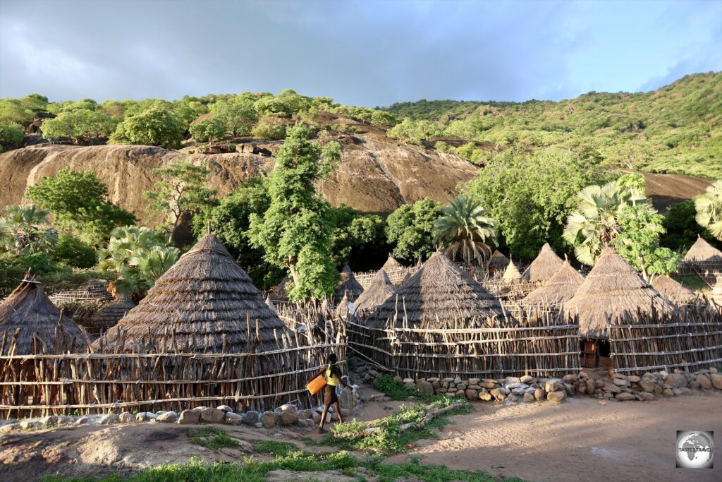 A young girl, on her way to collect water from a source high up on the rock in the background.