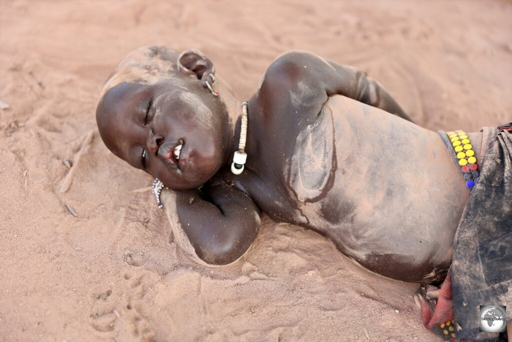 A Mundari baby, covered in cow-dung ash to protect against mosquito bites, sleeping on the ground.