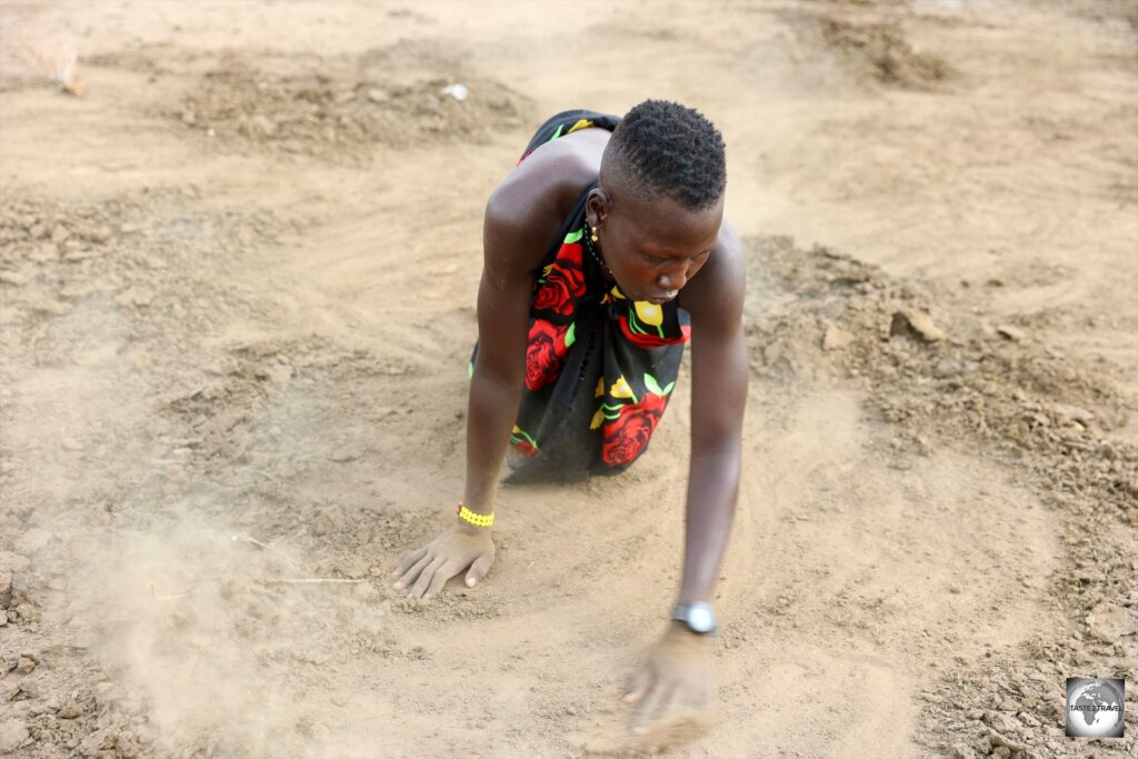 A Mundari girl, gathering cow dung which will be burnt on one of the many camp fires.